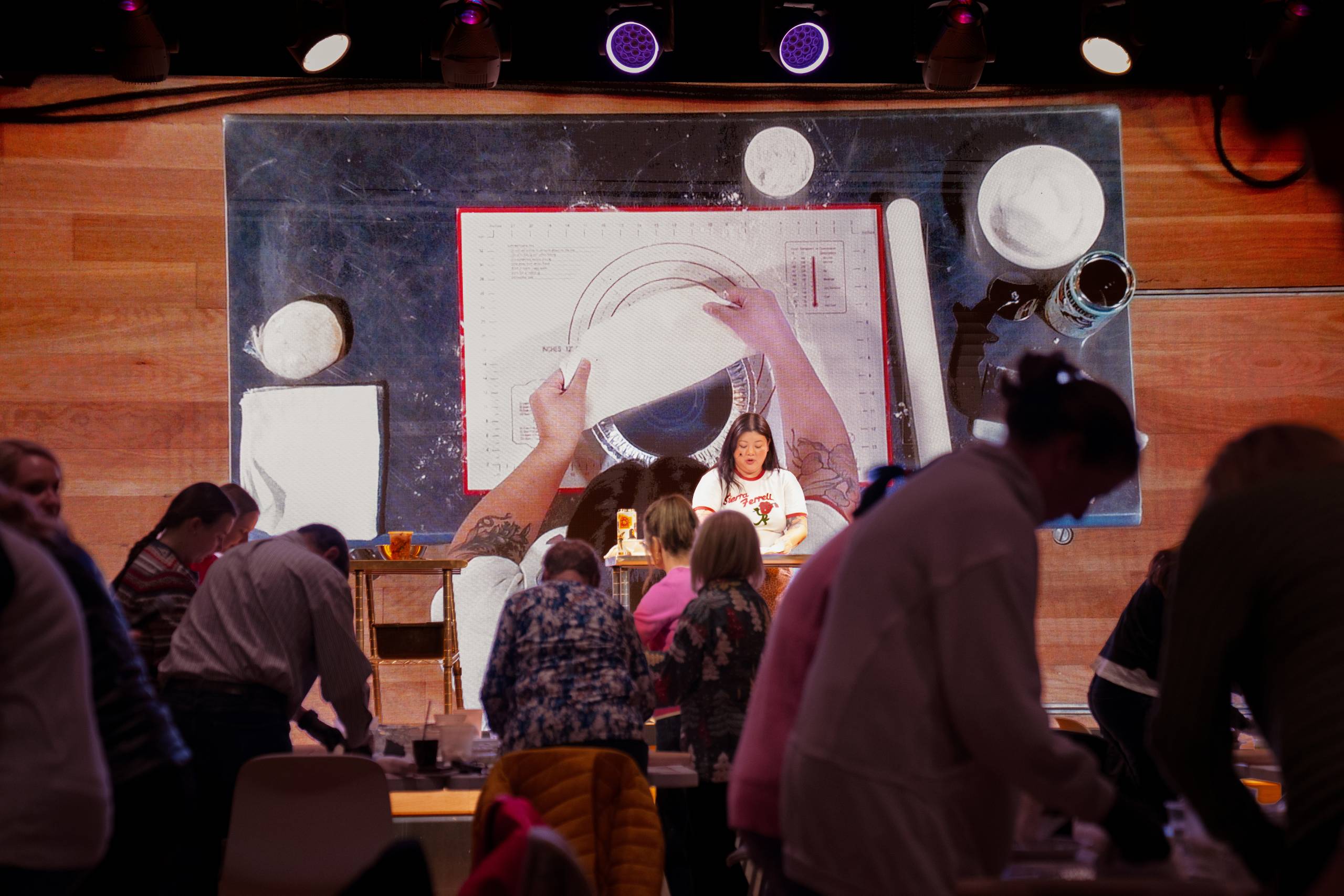 Top-down baking demonstration on large screen with people watching in workshop setting