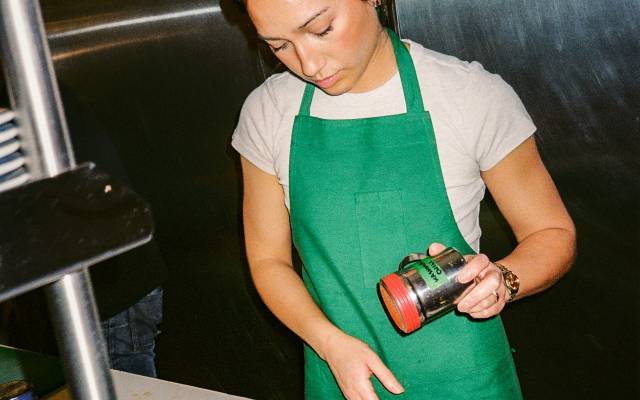 Woman in green apron sprinkling toppings on plated pastries in kitchen