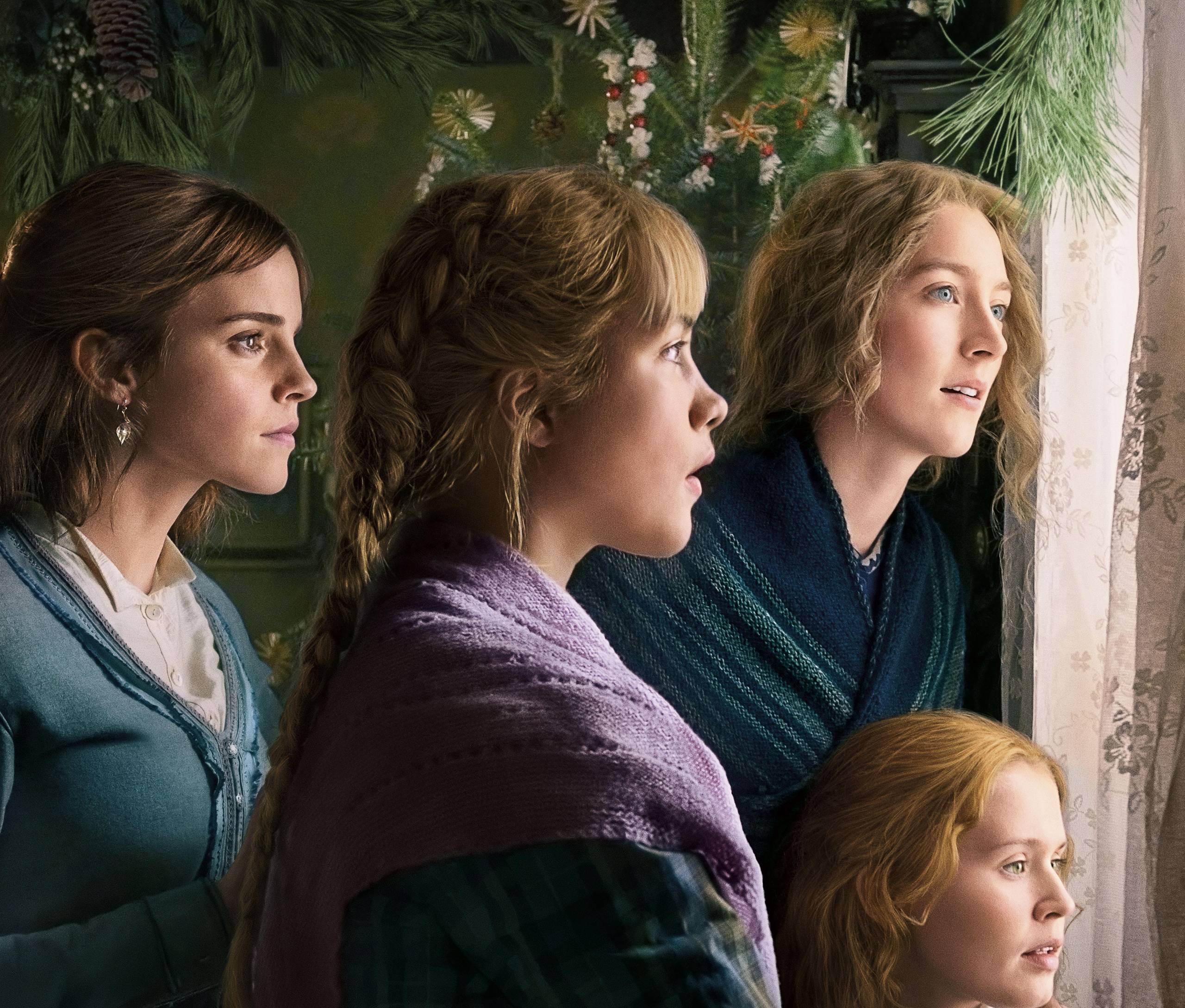 Four young women in sweaters stand by a window with Christmas greenery and decorations.