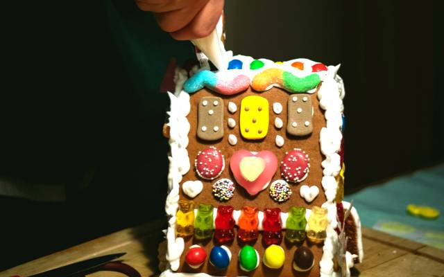 Person decorating a gingerbread house with icing and colorful candies on a wooden table.
